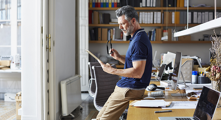 Side view of businessman using digital tablet while leaning on desk in office